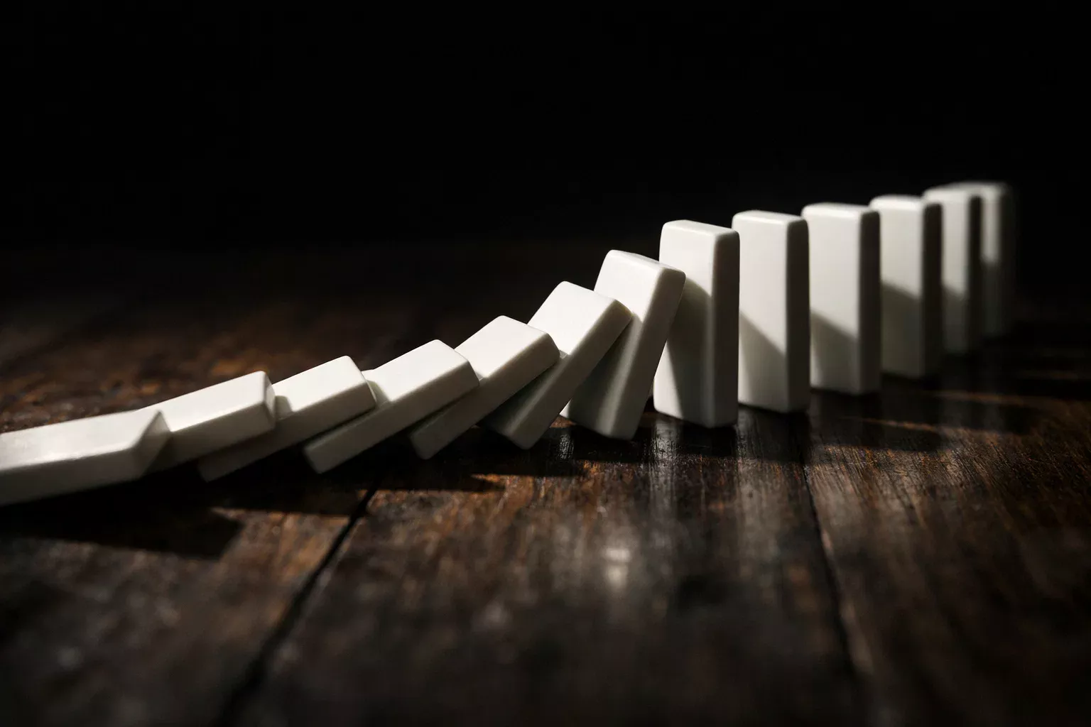 Rij dominostenen die omvalt op een donkere tafel als symbool voor ketenverlies