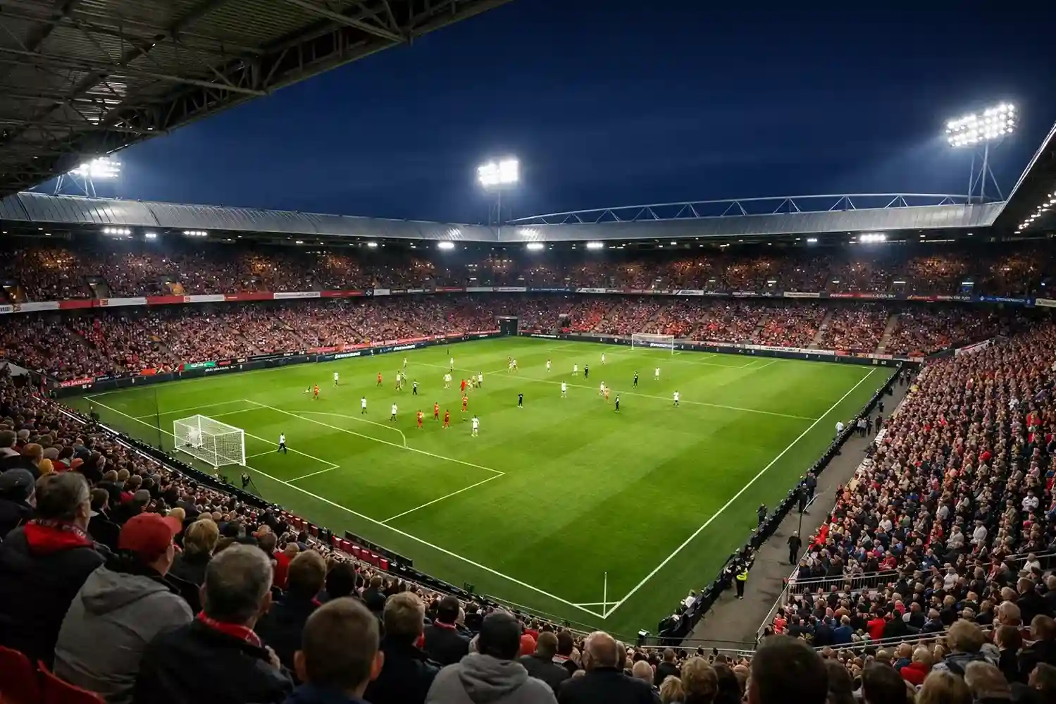 Nederlands voetbalstadion met groen veld en volle tribunes op een avond